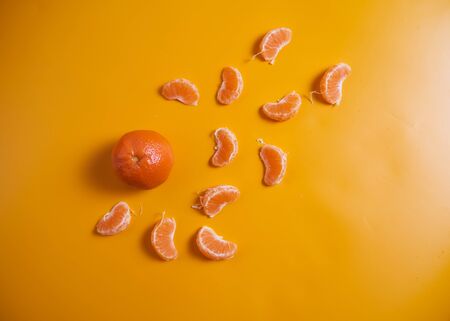 One whole tangerine with lots of slices on an orange background. High quality photo