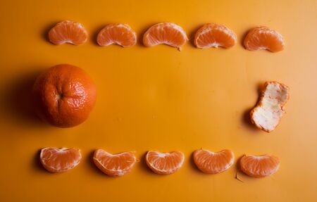 One whole tangerine and peel with lots of slices on an orange background. Concept photo. Top view....