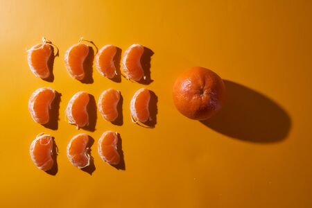One whole tangerine with lots of slices on an orange background. Shadow effect Concept photo. Top view.. High quality photoの写真素材