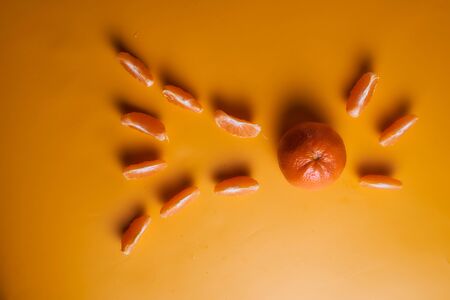 One whole tangerine with lots of slices on an orange background. High quality photoの写真素材