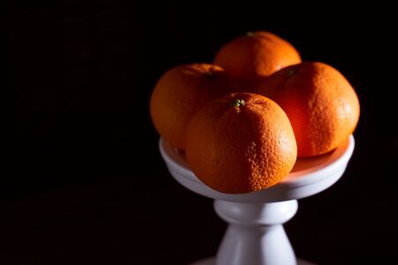 Four tangerines lie on a white stand. Black background. High quality photoの写真素材