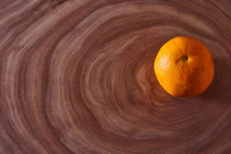 A orange mandarin lies on a slice of a tree. Wooden background. High quality photo
