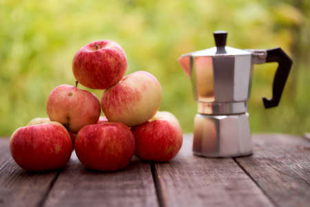 Geyser coffee maker stands on a wooden board against the green blurred background. With red apples. With copy space. High quality photoの写真素材