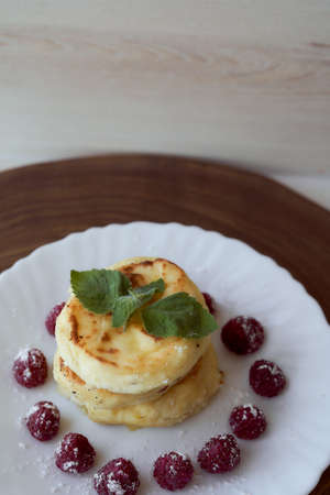 Juicy curd cheesecakes lie on a white saucer with raspberries and mint leaf. Light background. High quality photoの写真素材