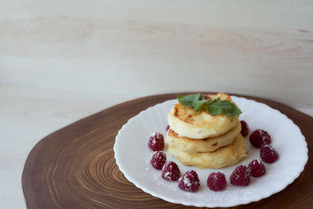 Juicy curd cheesecakes lie on a white saucer with raspberries and mint leaf. Light background. High quality photoの写真素材