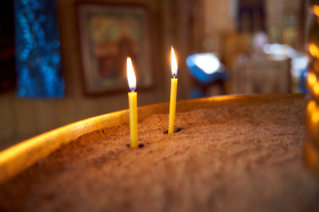 closeup of flame of a single burning red candle light in a dark chirch mourning symbolの写真素材