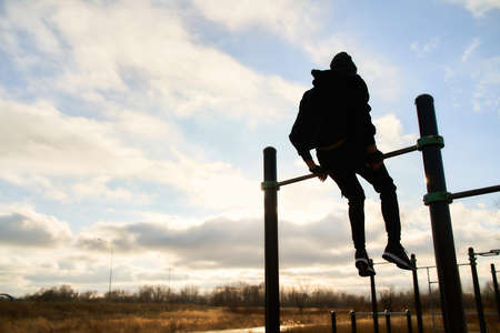 A young guy sits on the crossbar. Street sports playground. Sky background