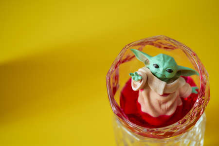 March, 2021: Display of Baby Yoda, an action figures, stands in a glass beaker with red liquid. Yellow background. High quality photoのeditorial素材