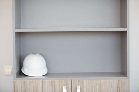 A white construction helmet of a worker lies on the shelf of a furniture cabinet. High quality photoの写真素材