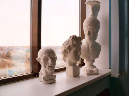 Plaster figures, busts stand on the window sill. Greek statues. High quality photo
