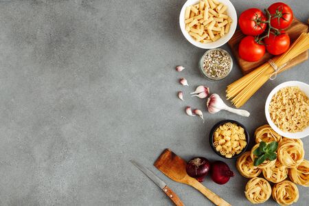 Spaghetti and fettuccine with ingredients for cooking pasta on wooden table with blank of wooden kitchen board, top view. Rustic style. Flat lay with empty spaceの写真素材