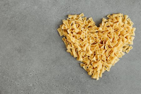Heart shape heap of farfalle or bow tie pasta isolated gray concrete backdrop. Flat lay with copy space, view from aboveの写真素材