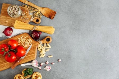 Spaghetti and fettuccine with ingredients for cooking pasta on cement backdrop with blank of wooden kitchen board, top view. Rustic style. Flat lay with space for textの写真素材