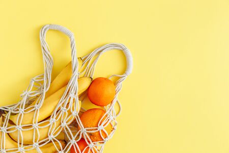 Sustainable eco friendly lifestyle. Cotton string mesh net bag with fruits. Reusable shopping tote for grocery with bananas and oranges on yellow background with copy space, ecological zero wasteの写真素材