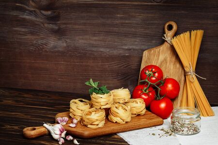 Raw spaghetti and fettuccine with ingredients for cooking pasta on wooden table with blank of wooden kitchen board. Rustic style. Copy spaceの写真素材