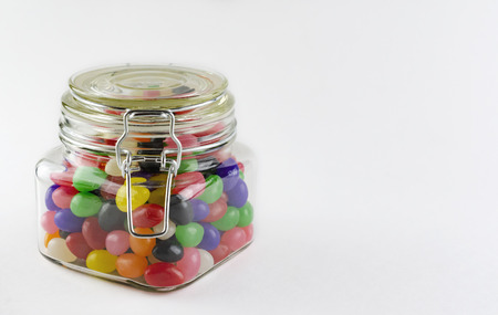 An assortment of jelly beans in a glass jar with clasp lid.  Isolated on white background.  Copy space on right side.の写真素材