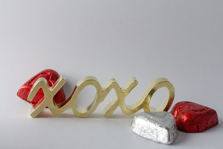 Gold symbol for hugs and kisses with three wrapped chocolate hearts on a white background.