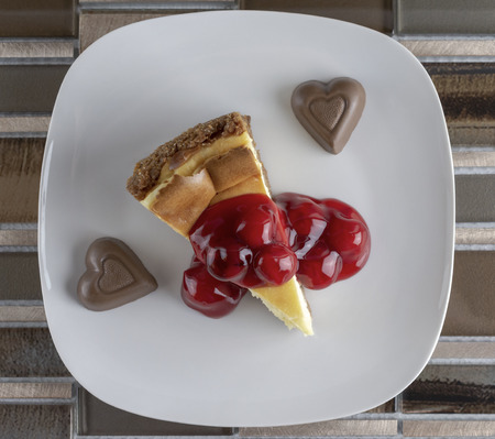 Flat lay of Cherry Cheesecake with two chocolate hearts on a brown tiled background.の写真素材