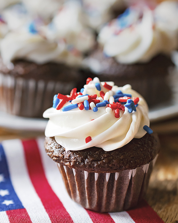 Close up of mini cupcake decorated with red, white, and blue sprinkles on a minature US flag.  Additional cupcakes blurred in the background.の写真素材
