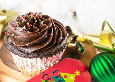 A Chocolate Christmas cupcake sits on a board surrounded by gift tag, bows, ornaments, and a Santa.の写真素材