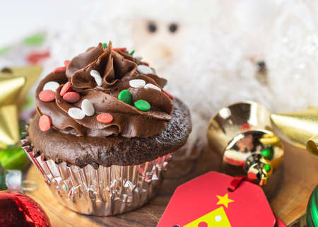 A Chocolate Christmas cupcake sits on a board surrounded by gift tag, bows, ornaments, and a Santa.の写真素材