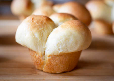 Close up side view of a freshly baked clover leaf dinner roll on a bamboo cutting board.  Additional rolls blurred in the background.の写真素材
