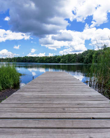 Looking down the boat pier on Genesee Lake in Waukesha County, Wisconsin.  Lazy cumulus clouds are reflected in the calm lake waters.の写真素材