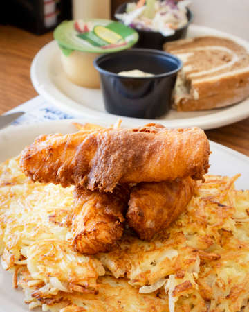 A traditional Wisconsin Friday night fish fry from a diner including deep fried cod, coleslaw, marbled rye bread, applesauce, cola, tartar sauce and hash browns.の写真素材