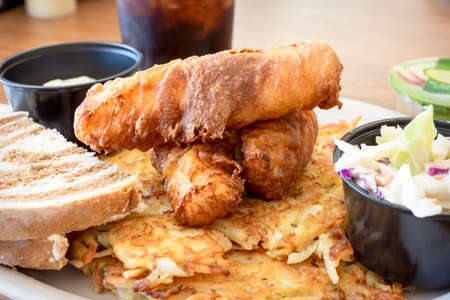 A traditional Wisconsin Friday night fish fry from a diner including deep fried cod, coleslaw, marbled rye bread, applesauce, cola, tartar sauce and hash browns.の写真素材