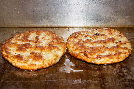 A pair of sausage patties cook on a flat grill in a restaurant.の写真素材