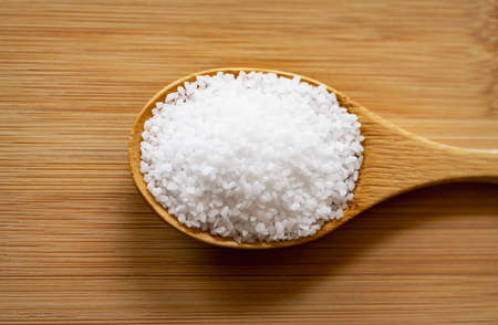 Coarse pretzel salt is piled onto a bamboo wooden spoon laying on a bamboo cutting board.