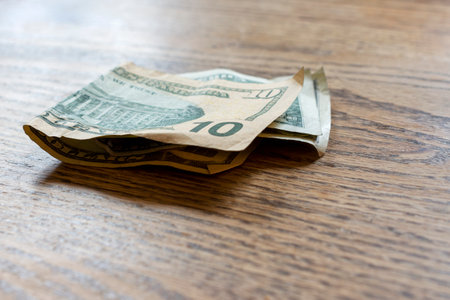 $10 and $1 of US money sits folded on a wooden table.
