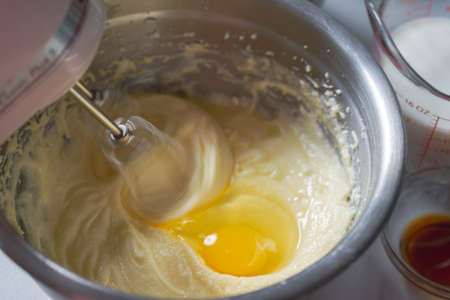 Making of a cake: Adding an egg and beating batter.  Mixer beaters showing motion blur.  Milk and...