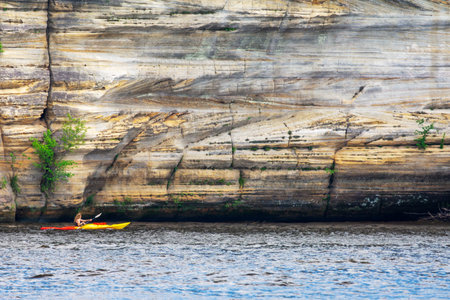 A kayaker paddles past some Cambrian sandstone bluffs along the Wisconsin River in the Wisconsin Dells.の写真素材