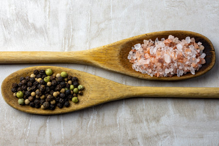 A pair of wooden spoons on a neutral tile background.  Rustic spoons are filled with Himalayan salt and peppercorns.の写真素材
