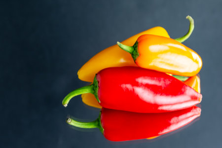 An assortment of red, orange and yellow sweet peppers on a mirror with a dark background.