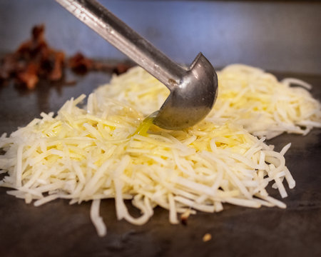 A chef uses a ladle to pour melted butter over shredded hash browns cooking on a hot flat-top griddle, preparing a savory breakfast.の写真素材