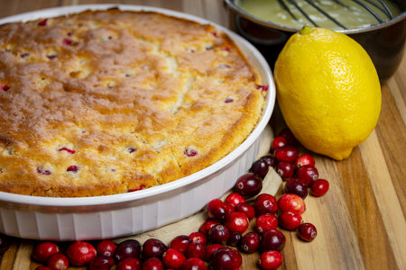 Whole baked cranberry cake with lemon glaze ingredients: saucepan, whisk, and fresh lemon slices....