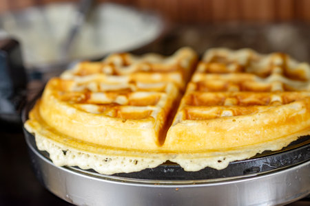 A golden-brown waffle, perfectly cooked with deep crevices, rests atop the open waffle iron after...