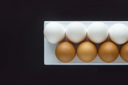 Fresh chicken egg in container on black paper background. Concept for Easter with copy space. White...