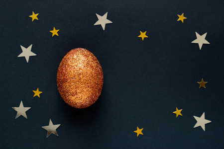 Brilliant egg with copy space for text on dark background with shine lights stars. Top view concept with bronze egg in flat lay style. Idea for greetings and Easter.の写真素材
