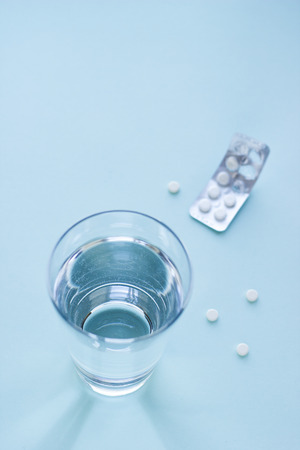 Tablets in blister pack and glass of water on blue background. Healthcare and medical concept with copy space. Top view.の写真素材