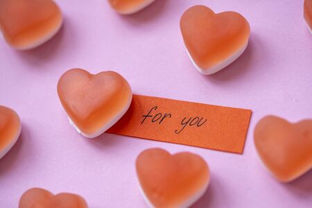 Red candy marmalade in shape of heart with a note FOR YOU on pink background. Sugar gummy candy....