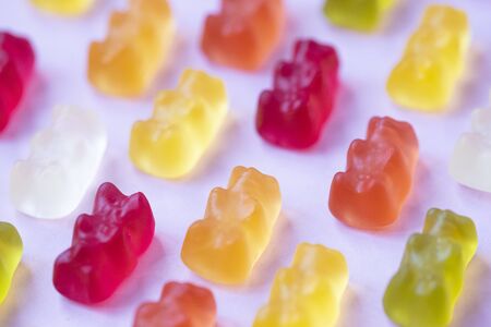 Colorful gummy bears on pink background. Orange, red and yellow jelly bears. Candy marmalade food. Geometric pattern. Minimal design, flat lay, top view.の写真素材