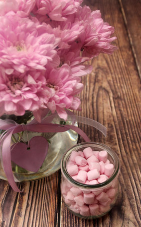 Pink heart shaped marshmallows in a glass jar and pink flowers on wooden backgroundの写真素材