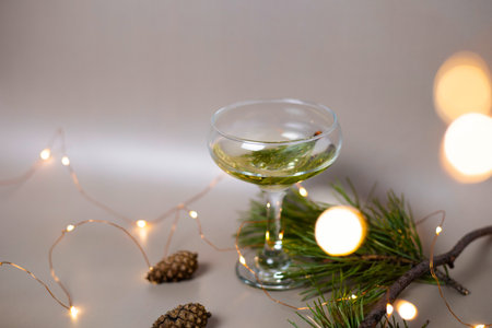 A glass of champagne surrounded by fir branches and cones on a beige background. Cocktail for the New Year. For the design of cards, invitations, posters, illustrations, presentations, flyers.の写真素材
