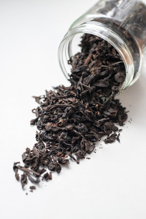 Jars with scattered tea leaves on a white surface. Traditional black tea. Dry herbal drink with...