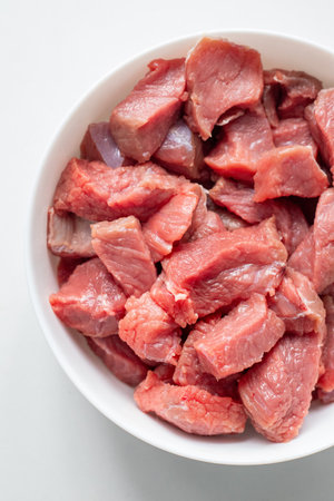 Raw meat in a white bowl on a white background. Red meat products. Finely chopped pieces of beef for cooking. Fresh ingredients for marinating and barbecueの写真素材