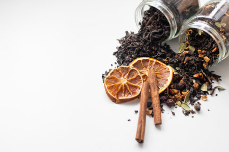 Black tea with orange slices and cinnamon sticks on white background. Tea leaves with fruit slices...