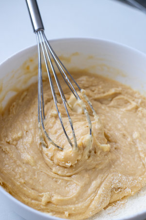 Kneading the raw dough with a metal whisk in a white bowl. Homemade baking and confectionery from...